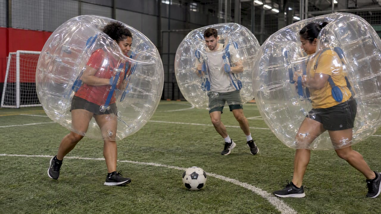 Teammates play bubble soccer on an indoor pitch