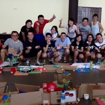 Group of people smiling and posing with hands raised, surrounded by creative projects